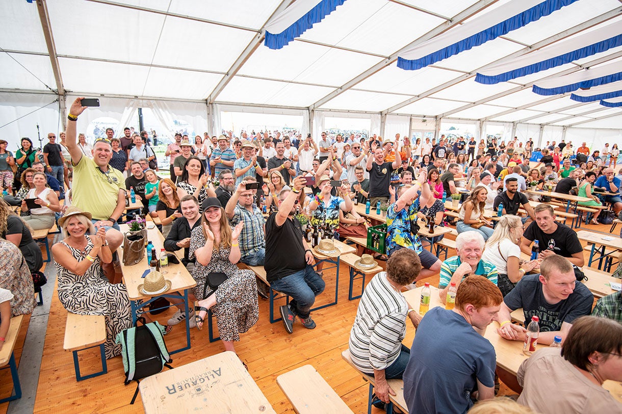 Crowd at Event in Large Tent with Wooden Benches
